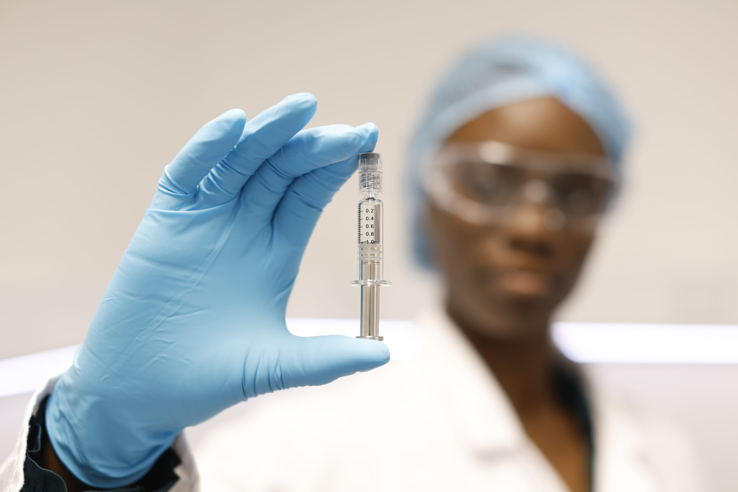 An out of focus process scientist in full GMP cleanroom PPE, showing a close up of a syringe containing pharmaceutical-grade EU-GMP dronabinol API manufactured by Dunbar Pharma.